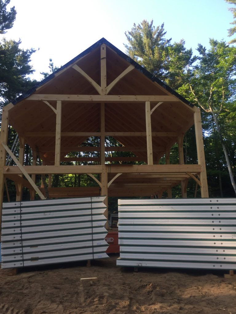 Front of the timber frame structure with a stack of SIPs in front